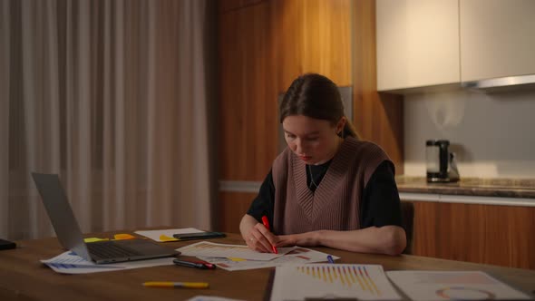 Side View A Woman Works Remotely in a Home Office at a Desk with a Laptop and Notes Data on a Graph alt