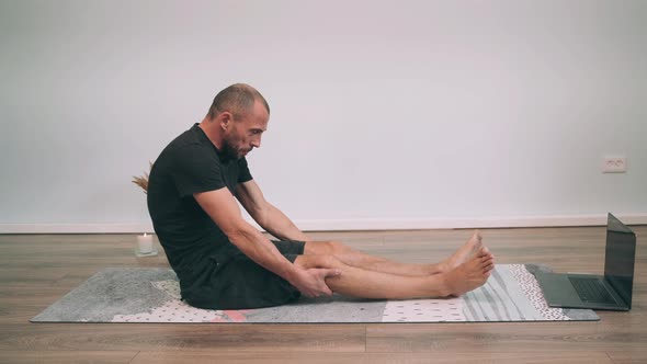 Caucasian Man Does Yoga Online Man Sits on the Mat and Does Forward Bends Man Performs Exercise and