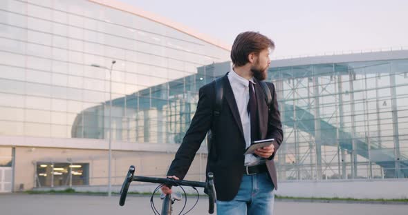 Office Manager Going with His Bike Near Urban Glass Building and Using i-pad alt