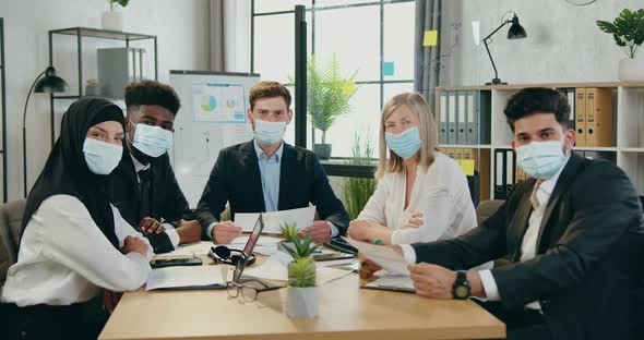 Multiracial Businesspeople in Protective Masks Looking Into Camera in Office Room alt