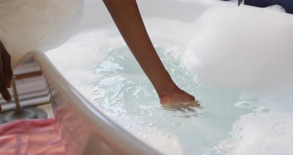 African american woman with towel preparing bath and touching water in bathroom alt