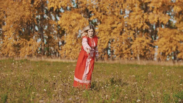 Strong Woman in Red National Dress Standing on the Field and Fencing with a Sword - Throws It Up and alt