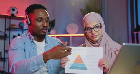 Man and Woman Sitting in front of Laptop in the Evening from Office During Video conference alt
