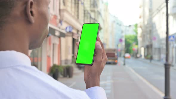Rear View of African Man Looking at Smartphone with Green Chroma Screen alt