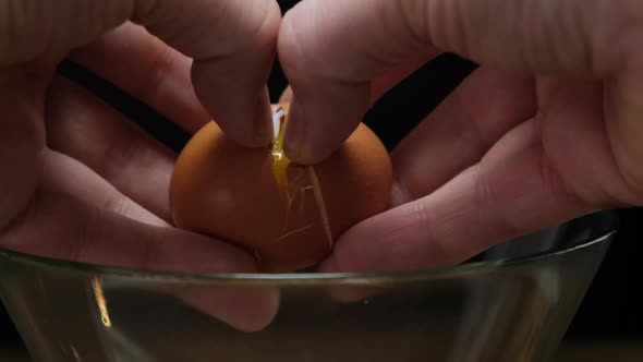 Hands holding one brown organic egg. Cracking over glass bowl. Close up. 4k