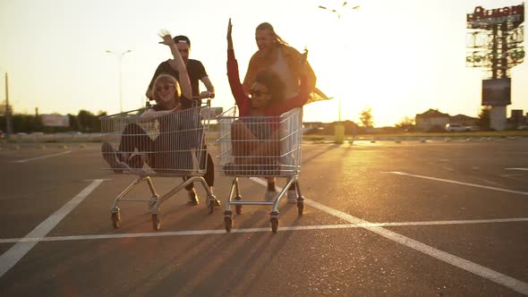 Multiethnic Friends Entertaining in Mall Parking Lot in Bright Day Racing with Shopping Cart alt