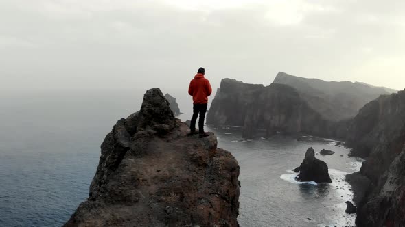 Drone Circle Around Man Hiker Standing on a Dangerous Cliff with Ocean View