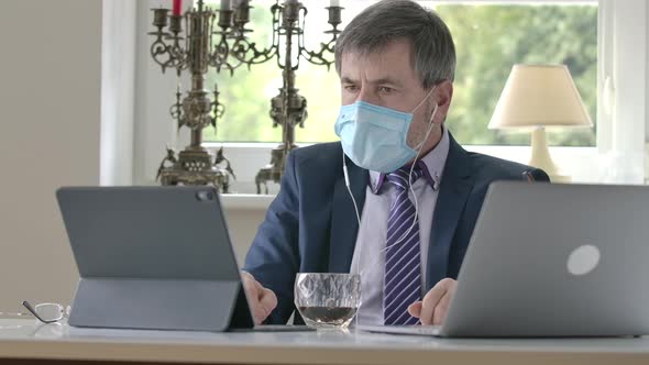 Confident Caucasian Businessman in Face Mask Sitting at the Table with Laptop and Tablet and alt