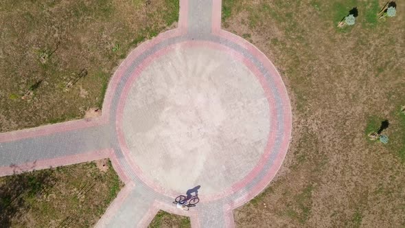 Top view of a bicycle woman riding a bicycle on a circular road in a city park. alt