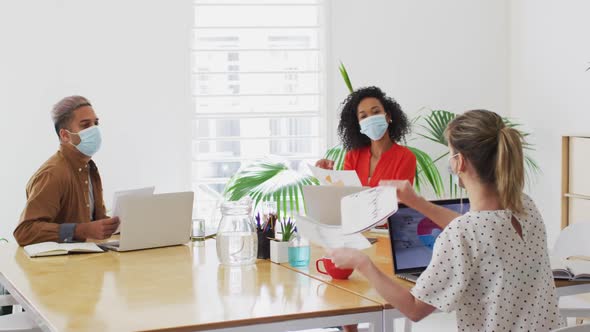 Woman wearing face mask showing a document to her colleague at office alt