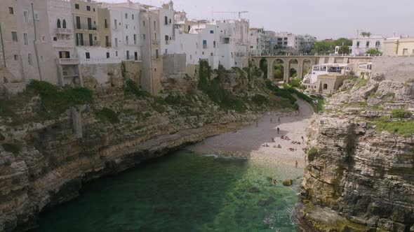 Slow aerial flyover of Lama Monachile beach in Polignano a Mare, Italy with sea and cliffs and waves alt