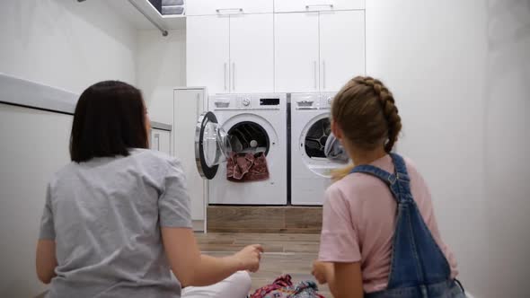 Young Woman and Her Daughter Having Fun While Doing Laundry at Home Throwing Clothes Into Washing