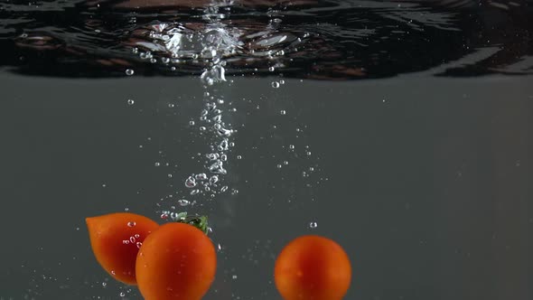Closeup of Fresh and Health Cherry Tomatoes Falling Into Clear Water with Big Splash on Black alt