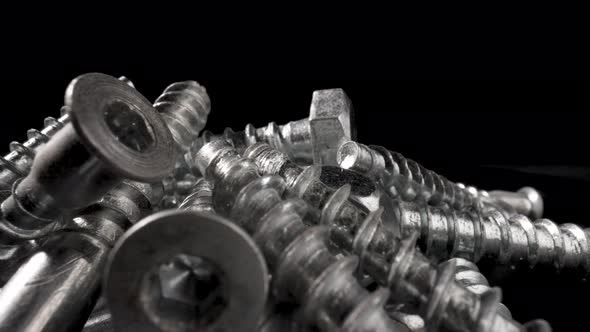 Pile of Steel Chrome Screws Rotating on Isolated Black Background alt