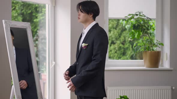 Side View of Elegant Asian Groom in Wedding Costume Entering Living Room Walking to Window Looking alt