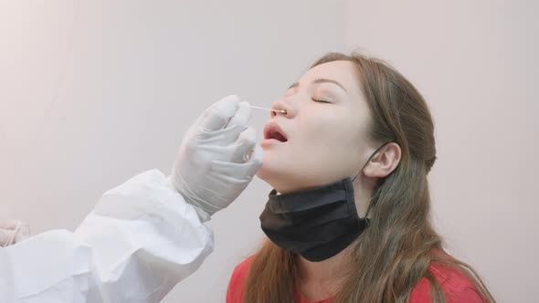 Anonymous doctor putting a cotton stick into nostril of an asian girl for laboratory COVID-19 alt