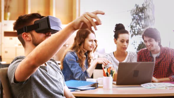 Male business executive using virtual reality headset while colleagues interacting at desk alt