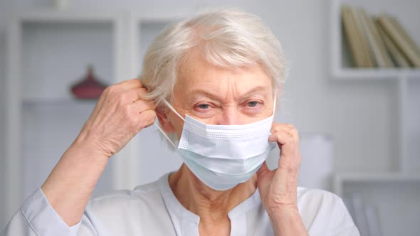 Old woman manager takes white disposable face mask off alt