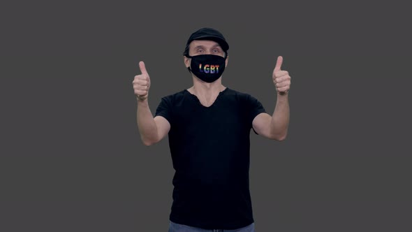 Gay man in anti covid lgbt mask looks at camera and gesturing, Alpha in