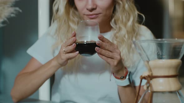 Young blonde woman enjoying taste and smell of Americano in a coffee shop. alt