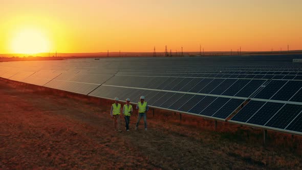Aerial Zoom Out Shot of Workers Walking About Solar Farm at Sunset alt