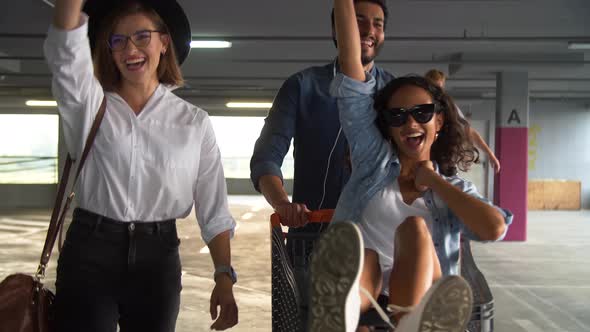 Young People Having Fun, Racing On Shopping Trolley At Parking alt