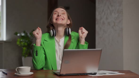Woman with Headphones on Neck Gets Happy Looking in Laptop alt