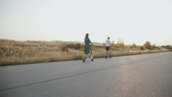 Couple in Love Riding Fast to Sunset on Electric Scooters with Joy on a Road alt