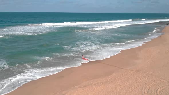 Aerial shot of distant person heading out from beach with red kayak alt