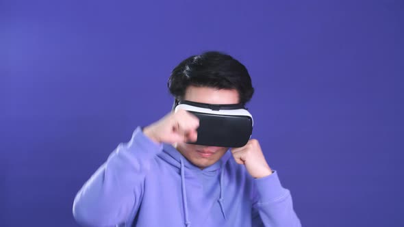 Young Asian Man Playing VR Game in Dark Blue Background. Chinese Young Hipster Wearing VR Headset. alt
