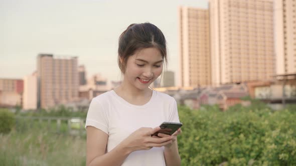 Asian tourist blogger woman using touchscreen technology at smartphone while walking. alt