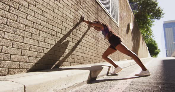 African american woman exercising outdoors leaning of wall and stretching in the city alt