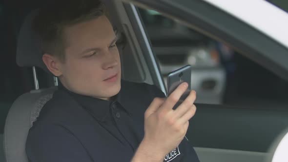Young Cop Chatting in Social Networks on Smartphone Sitting in Police Car alt