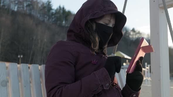 Girl in a Mask Outdoors Uses a Tablet. Insulation