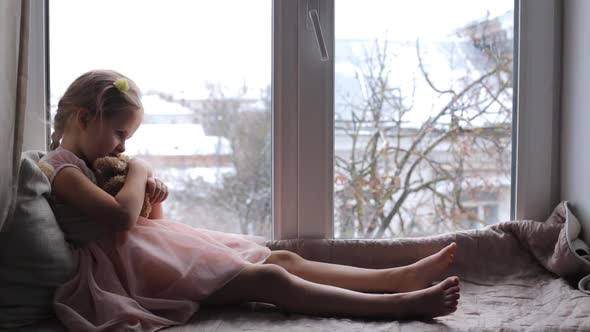 Little Child Sits on a Windowsill with a Teddy Bear alt
