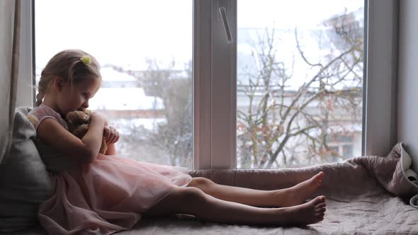 Little Child Sits on a Windowsill with a Teddy Bear