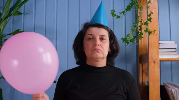 Lonely Unhappy Sad Woman in Cap Looking at Camera and Holding Balloons Celebrating Birthday Alone