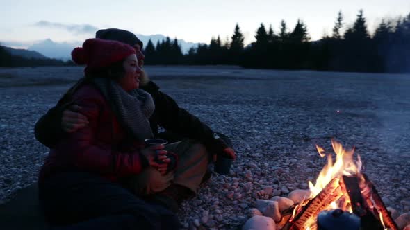 Group of friends sitting at a bonfire at dawn alt