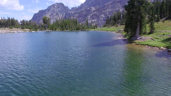 Camera flies over pond towards forest and a mountainside in the distance alt