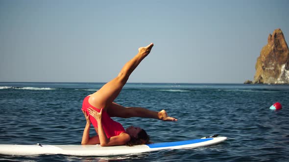 Young Woman in Red Swimsuite Doing Yoga or Pilates on Sup Board with Paddle alt