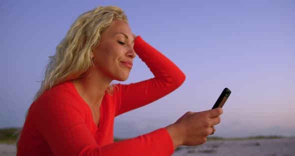 Woman using mobile phone on beach at dusk 