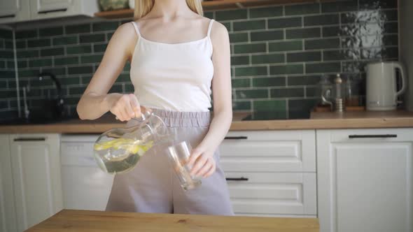 Beautiful Slender Woman Drinks Lemon Water in the Kitchen alt