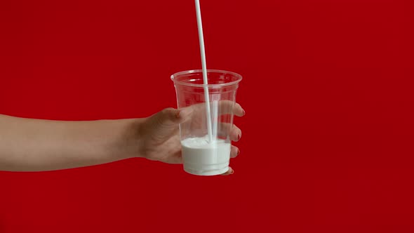 Wide View of Woman Hands Pouring Milk Into Empty Plastic Glass in Slow Motion alt