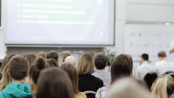 Viewers in Large Audience Photographing Man Speaker on Smartphones, Back View. alt