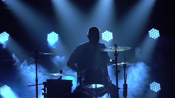 Silhouette Drummer Playing on Drum Kit on Stage in a Dark Studio with Smoke and Neon Lighting alt