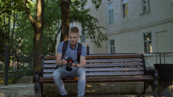 Tourist Sits on a Bench and Scrolls at the Photographs Taken on a Digital Expensive Big Camera. alt