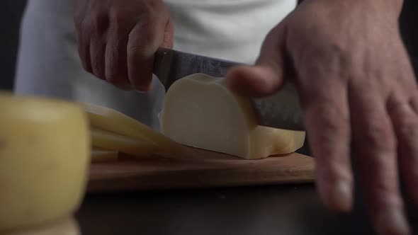Chef in Restaurant Kitchen Beautifully Cuts the Hard Cheese with a Large Knife.