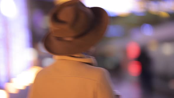 Stylish Woman in Hat and Coat Walks Through the Night City in Lights