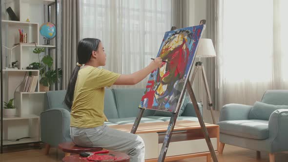 Asian Artist Girl Holding Paintbrush Mixed Color And Painting A Girl's Ear On The Canvas alt