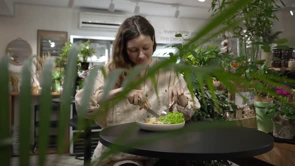 Woman Sits at Table in Cafe and Cuts Toast on White Plate alt